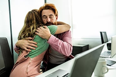 Två personer som kramas vid ett kontorsbord