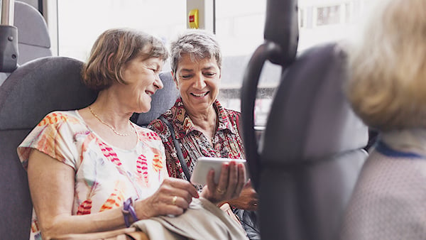 Två äldre kvinnor på buss tittar på samma mobil